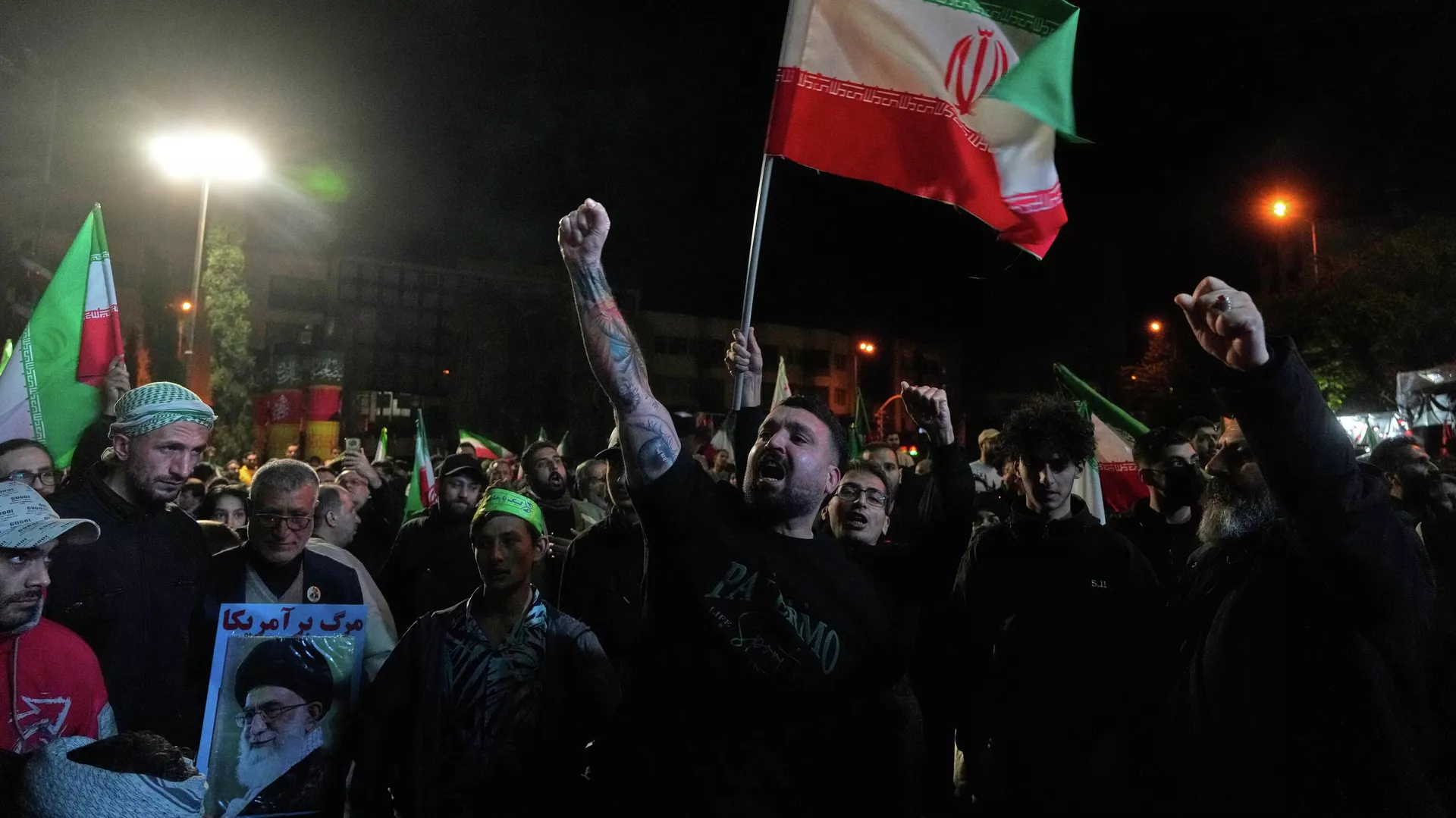 Demonstranți proguvernamentali scandând sloganuri, ținând steaguri iraniene și un banner cu portretul liderului suprem decedat, ayatollahul Ali Khamenei